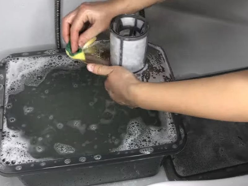 Osoba čisti u lavoru i kadi filter od mašine za sudove