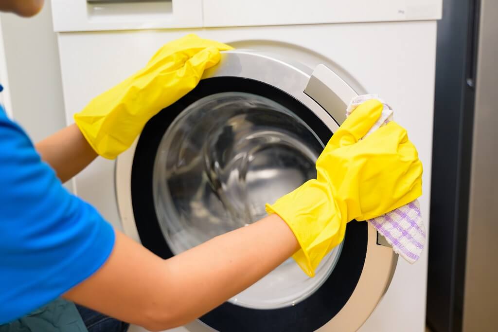 Osoba u žutim rukavicama briše spoljašnji deo vrata veš mašine krpom