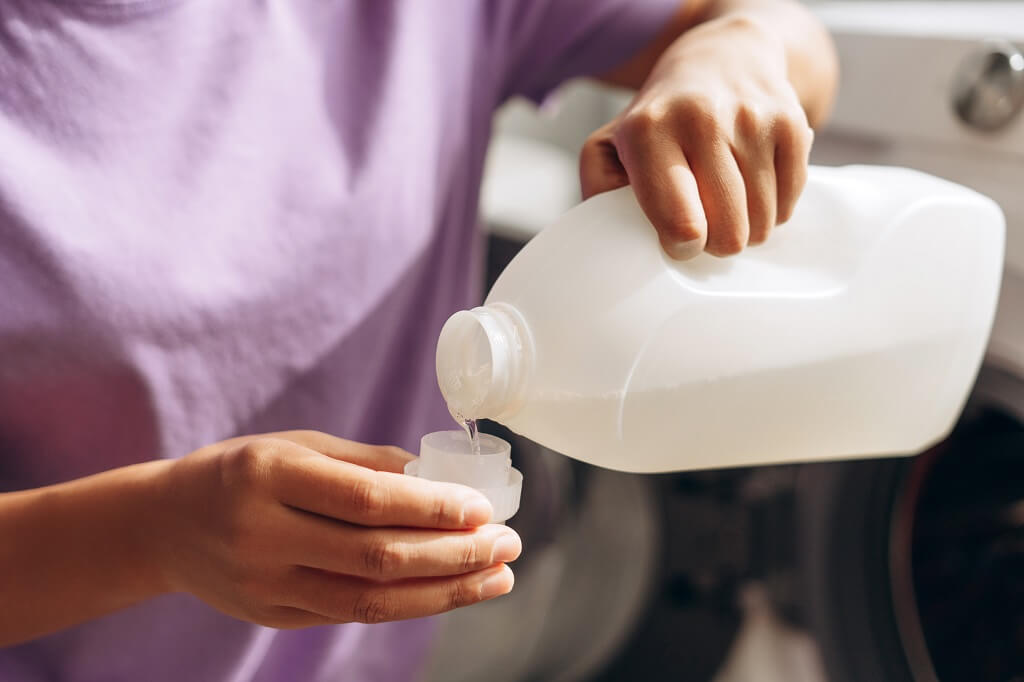 Ruka sipa sredstvo za čišćenje iz plastične boce u mericu ispred veš mašine